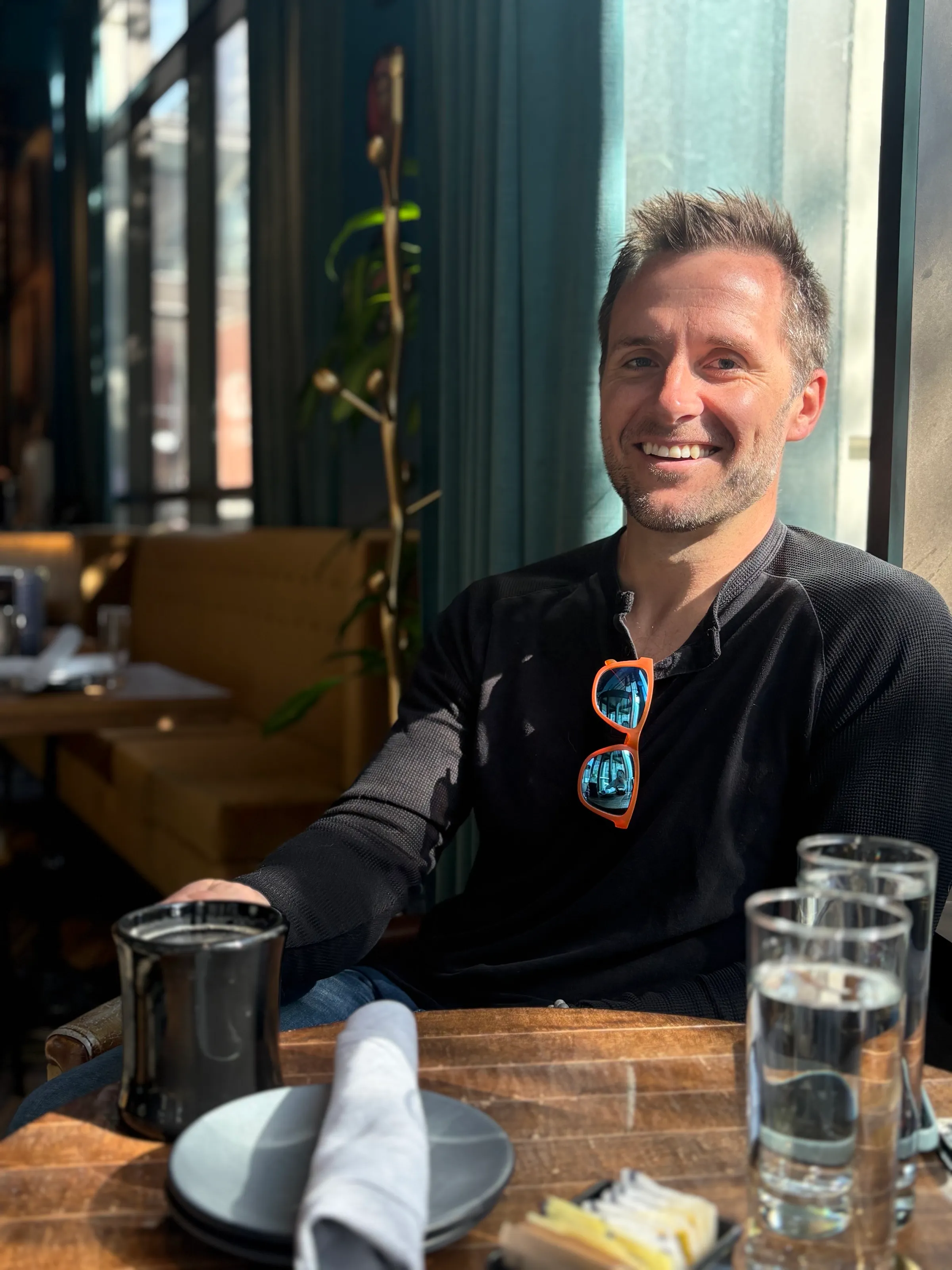Ryan Vaughn smiling at a cafe table in morning light